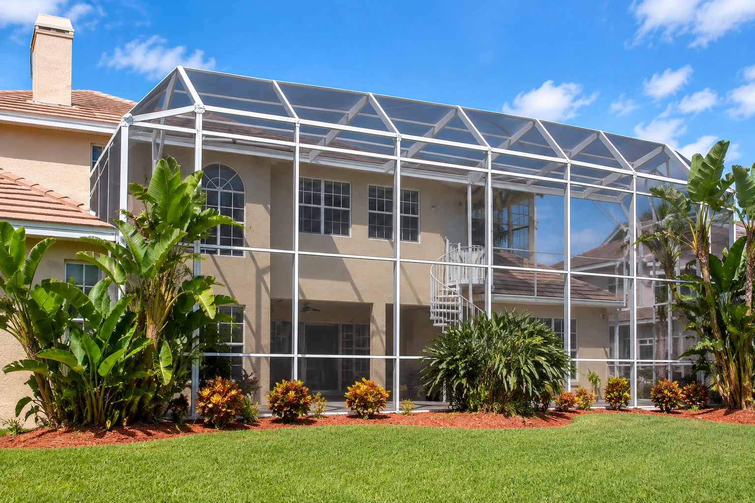 Large screened patio enclosure with a silver frame attached to a house, surrounded by tropical plants and lawn.