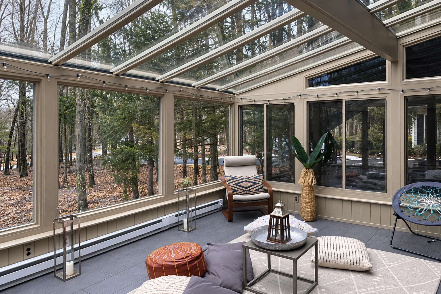 Four-season sunroom with a glass roof, beige-framed windows, and a lounge area facing a wooded yard.