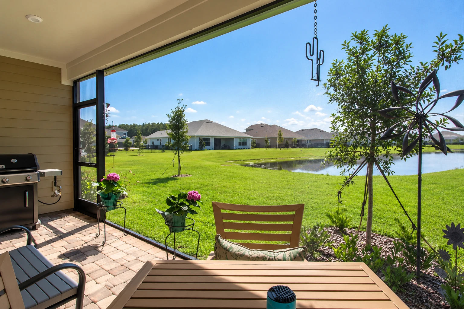 Enclosed patio with open glass walls, a barbecue grill, and seating overlooking a lawn and pond.