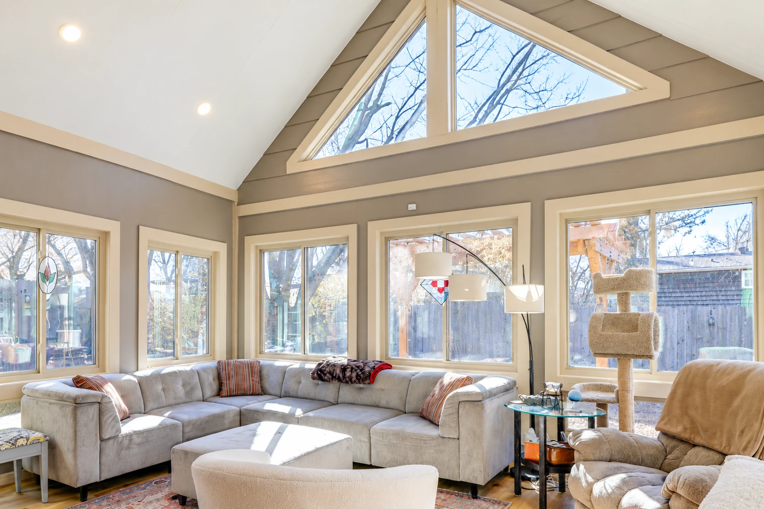 Bright sunroom living area with a high vaulted ceiling, triangular clerestory windows, and a large beige sectional.